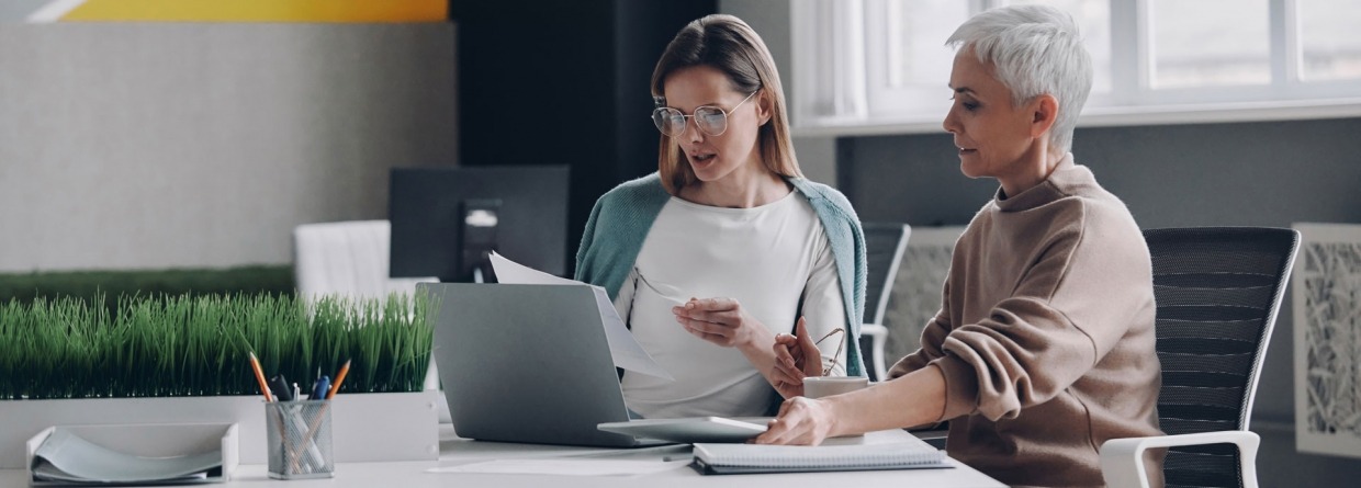 Twee zelfverzekerde vrouwen die technologieën gebruiken en communiceren terwijl ze samen op kantoor werken